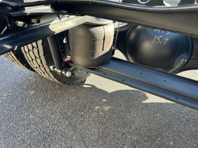 Cab and chassis undercarriage showing suspension components and a cylindrical air tank with 15.7 marking, along with frame rails and leaf springs.