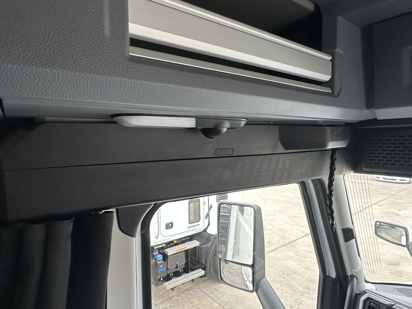 Cab interior area showing overhead storage with a metal dash insert and a small label, window mirror visible; no other legible text.