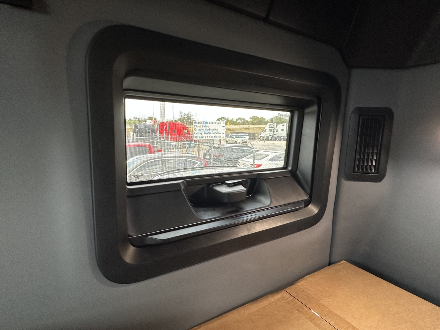 Cab interior side window view in a new Mack PR64T76H sleeper cab showing cargo area and small window.