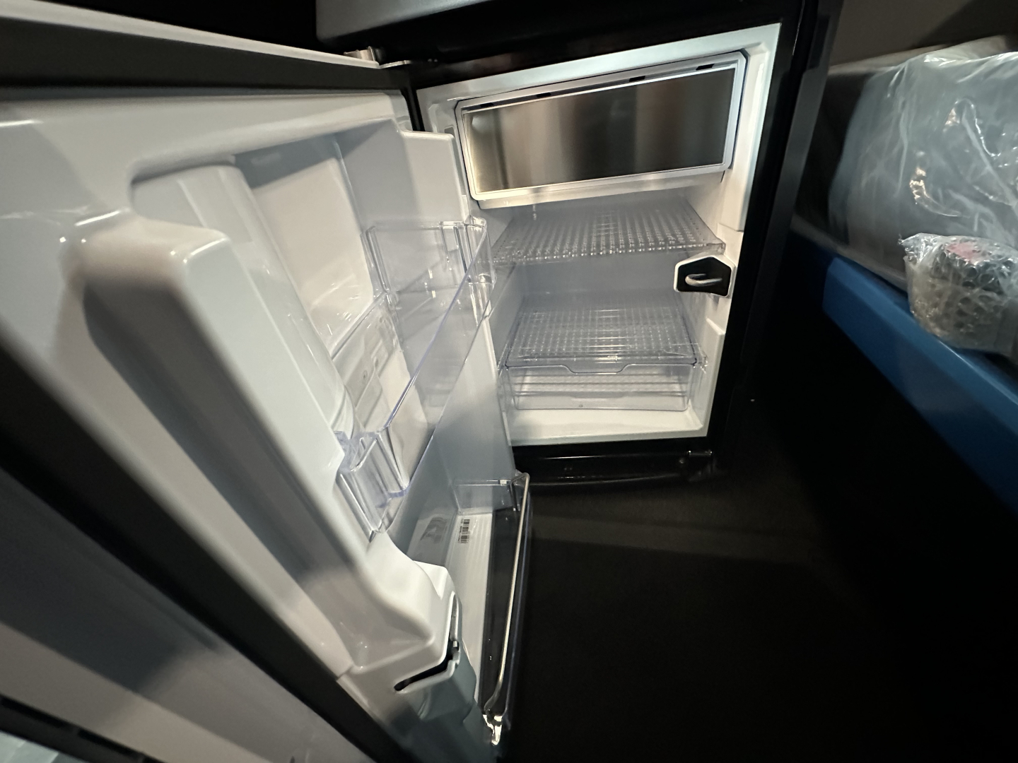 Fridge-freezer in cab of new Mack PR64T76H truck showing open small refrigerator/freezer unit inside with empty shelves.