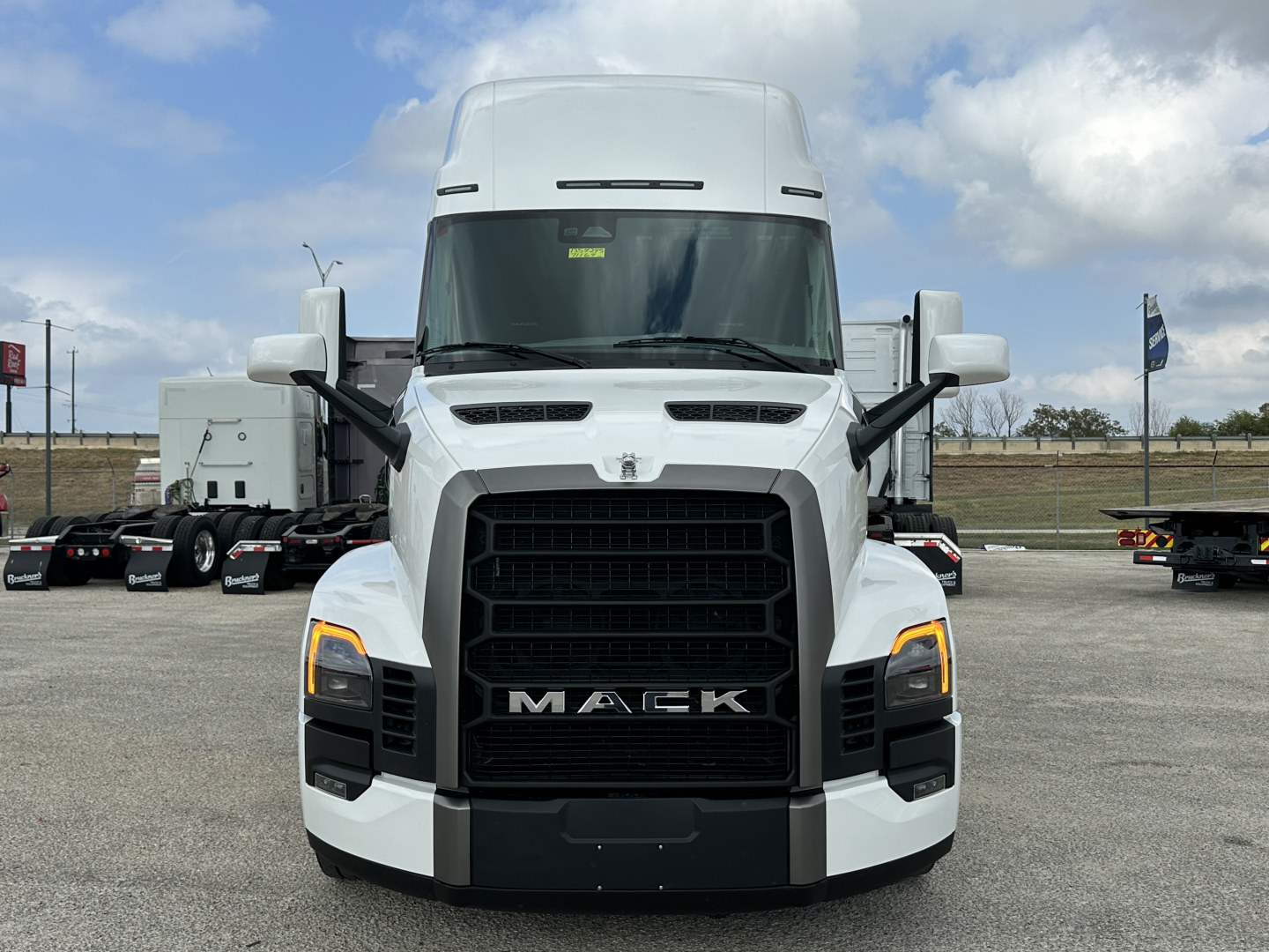 Mack PR64T76H truck front view showing bold black grille with MACK lettering, white cab, side mirrors, and headlights.