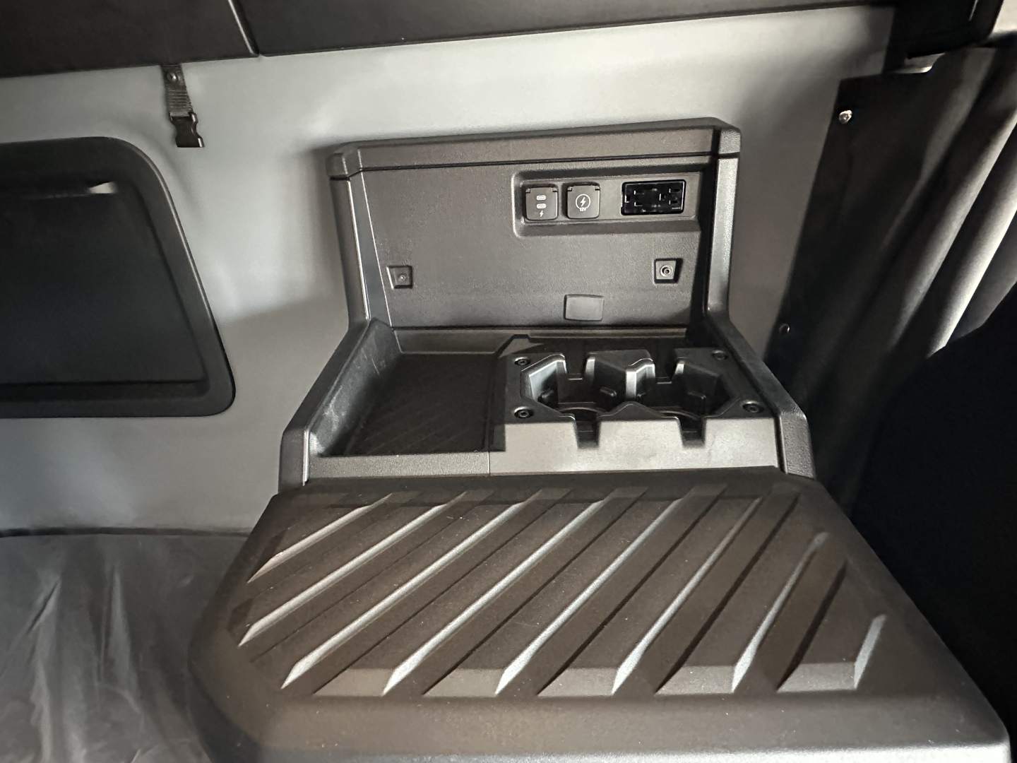 Truck cab interior center console with USB/12V outlets and storage, view into sleeper area showing control panel and cup holders.