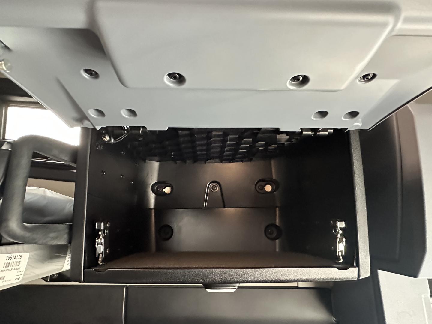 Truck cab storage compartment under dash showing empty electronics bay drawer with metal rails and latches in a Mack PR64T76H cab.