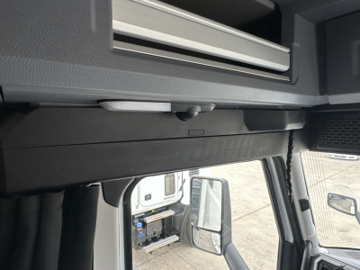 Cab interior area showing overhead storage with a metal dash insert and a small label, window mirror visible; no other legible text.