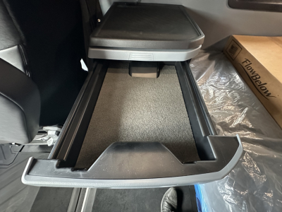 Truck interior center console open storage drawer with carpeted tray and side rails in cabin of 2026 Mack PR64T76H.