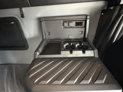 Truck cab interior center console with USB/12V outlets and storage, view into sleeper area showing control panel and cup holders.