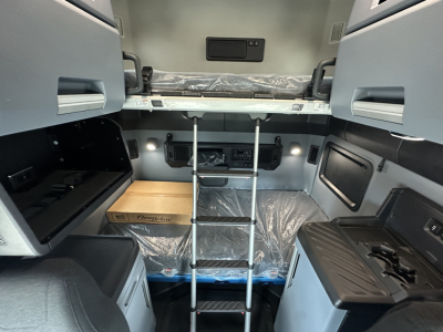 Cab interior of a new 2026 Mack PR64T76H sleeper with upper bunk, ladder, and storage compartments visible.