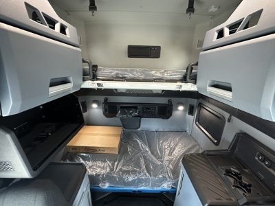 Truck cab interior with sleeper berth and overhead cabinets, control panel, storage compartments, and protective floor covering.
