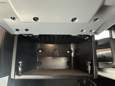 Truck cab interior showing open glovebox/storage compartment under dashboard; metal box with hinges and latches visible.