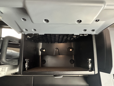 Truck cab storage compartment under dash showing empty electronics bay drawer with metal rails and latches in a Mack PR64T76H cab.