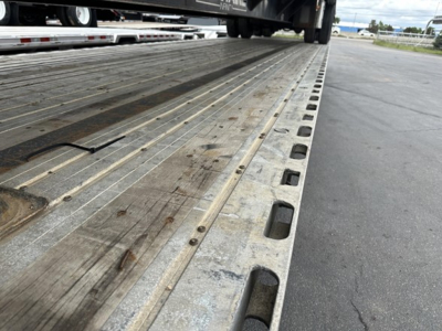 Trailer deck showing metal drop deck with tie-down slots and textured boards from low angle.