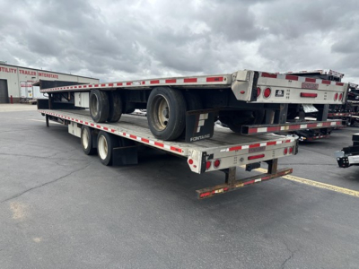 Flatbed trailer with rear slide axle showing Fontaine logo and decals; dual rear landing gear, tires, and safety rails visible.