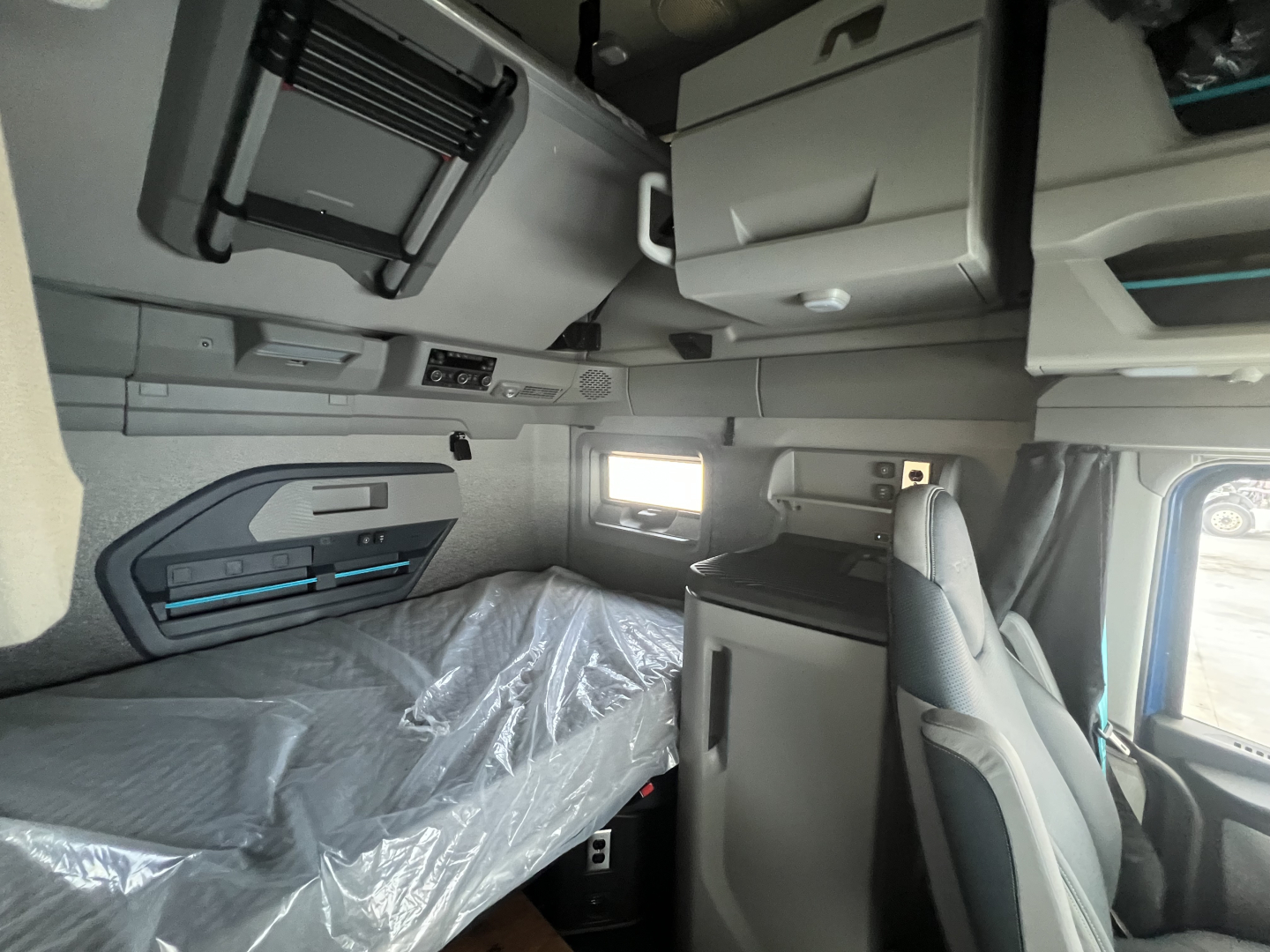 Interior cab of a Volvo VNL truck showing sleeper berth with overhead storage, window, and driver's seat; visible panels and compartments.