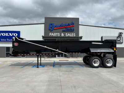 Dump trailer with black body and raised side rail, three-axle configuration, showing Bracken's Parts & Sales building in background.
