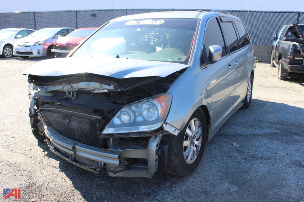 Front-left view of a damaged 2008 Honda Odyssey minivan showing a crumpled front bumper, exposed radiator area, and hood misalignment.