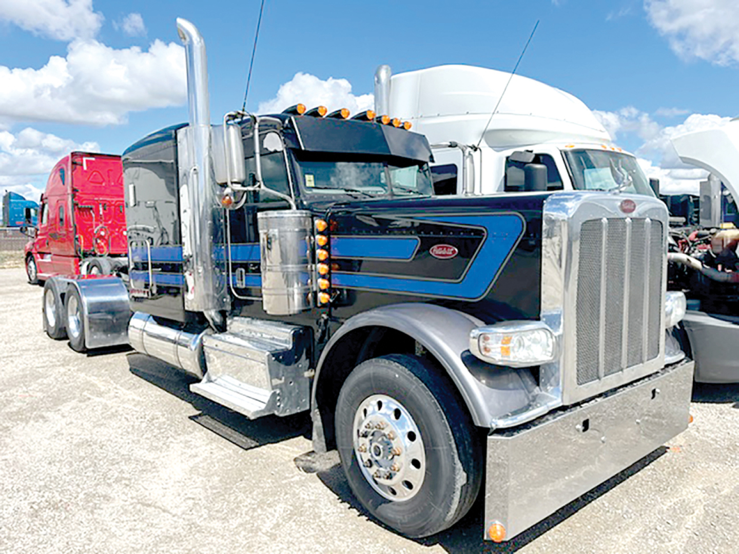 Peterbilt 389 extended hood semi-truck in a lot, front view with chrome exhaust stacks and blue/gray paint.