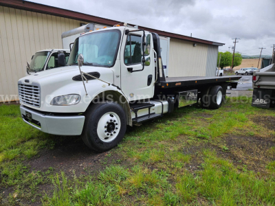 Truck side view showing 2015 Freightliner M2 106 with flatbed cargo area and dual rear wheels.