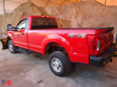 Ford F-350 Super Duty pickup with 4x4 badge visible, red long-bed crew cab, side view showing tire, gate and plow mounting area in a rocky indoor setting.