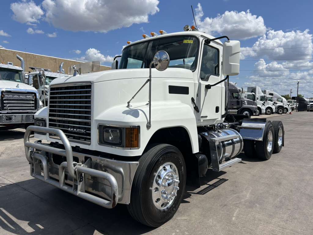 Mack PI64T conventional daycab truck in white with chrome bumper guard, dual rear axles, and fuel tanks visible.