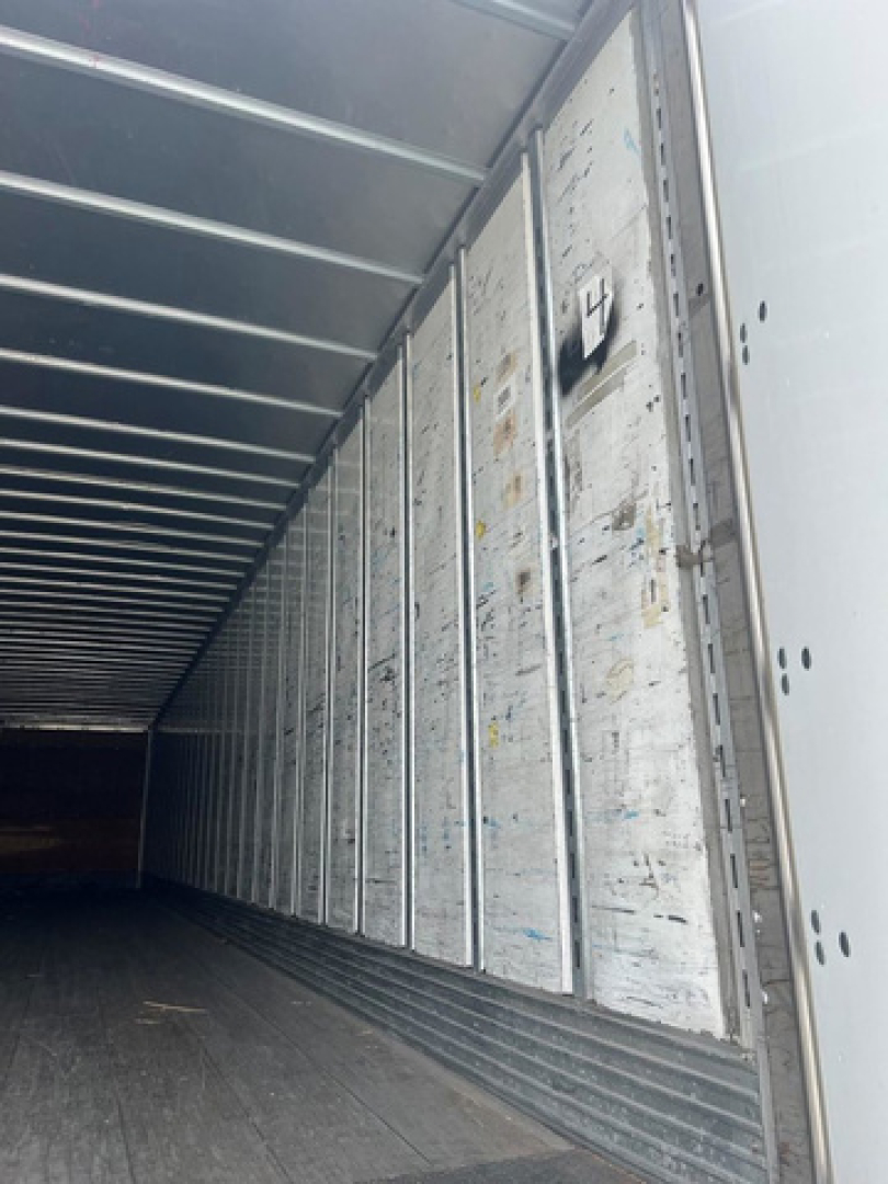 Interior of a utility van trailer showing metal side paneling, ribbed ceiling, and loading area with weathered panels.