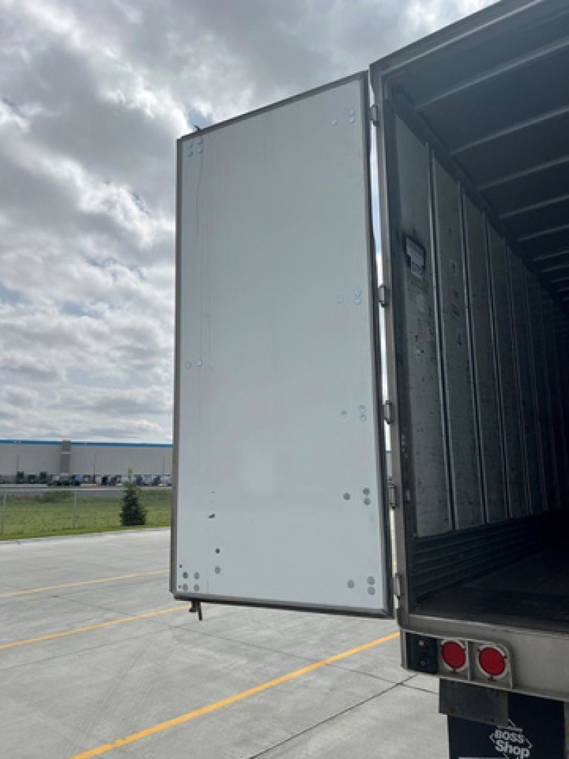 Rear door of a utility van/trailer open showing interior cargo space and door hinge area.