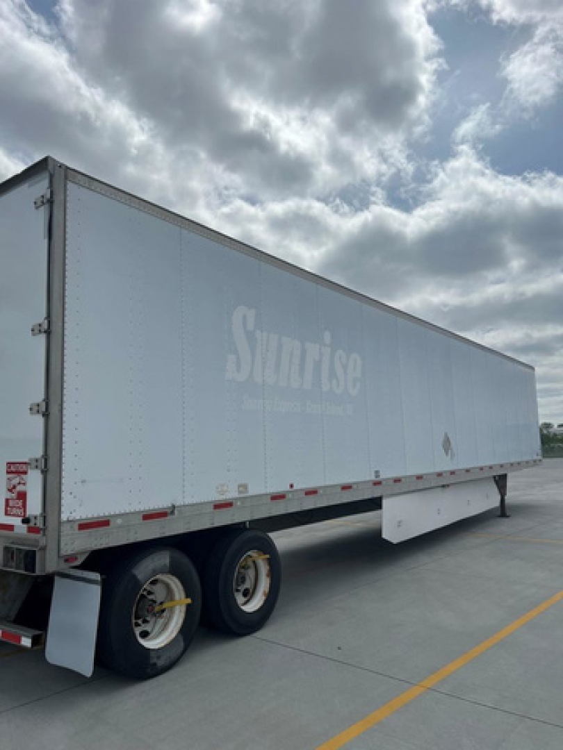 Trailer side of a light gray Sunrise trailer with a faint logo and dual rear wheels visible.