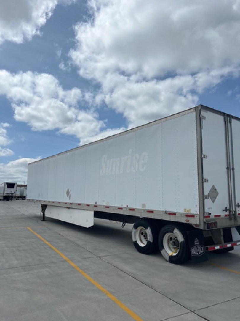 Trailer side view of a long white utility van trailer with dual rear axles and undercarriage, visible 'Sunrise' logo faded along the side.