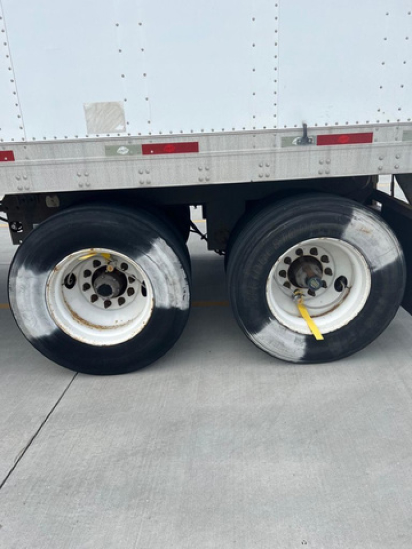 Trailer wheelset of a utility van showing dual rear axles with metal rims and tires; wheel hubs and lug nuts visible, part of a white refrigerated trailer side.