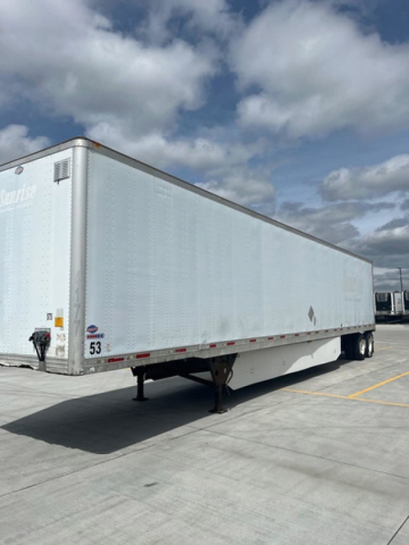 Trailer side view showing a white utility van trailer with landing gear and rear wheels visible; stock number 53 plate and DOT markings near front corner.