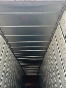 Van trailer interior showing long narrow cargo area with ribbed metal walls and ceiling, viewed from rear doorway.