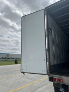 Rear door of a utility van/trailer open showing interior cargo space and door hinge area.