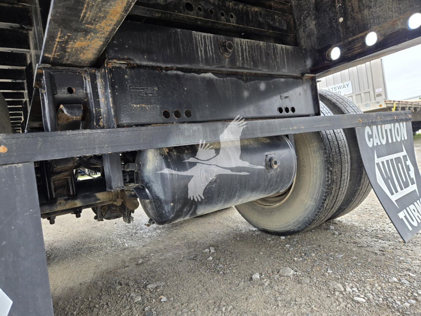 Trailer undercarriage showing steel frame and flatbed support with wheel and axle visible.