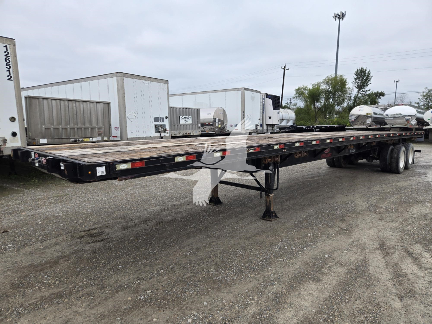 Flatbed trailer showing long low-profile deck and tandem axles with landing gear, VIN 5JYFB4820JED06769 visible on frame.