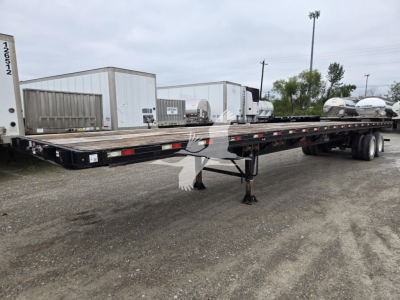 Flatbed trailer showing long low-profile deck and tandem axles with landing gear, VIN 5JYFB4820JED06769 visible on frame.