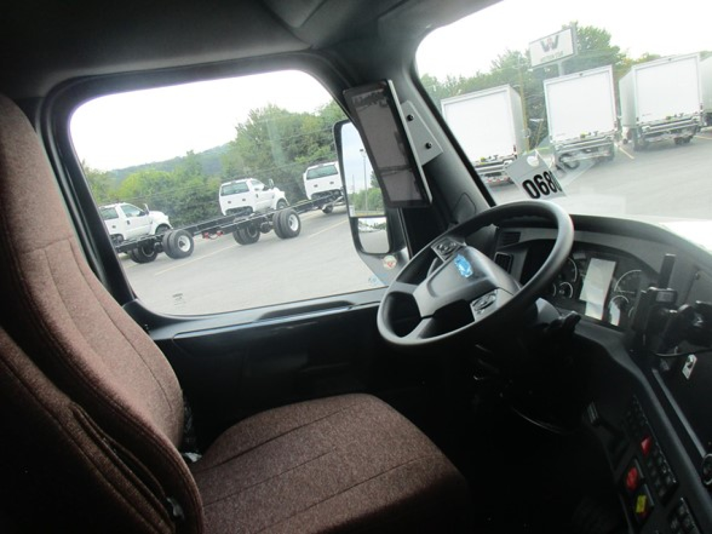 Truck cab interior showing steering wheel and dashboard of a Freightliner Cascadia 126 with brown seat fabric.