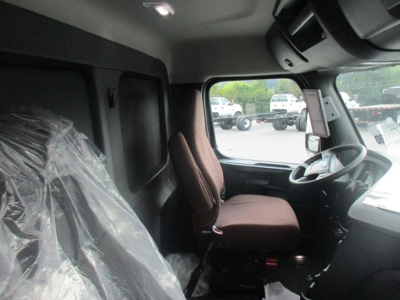 Truck cab interior showing steering wheel and driver seat in a Freightliner Cascadia 126, with plastic-covered seat on left and dashboard visible.