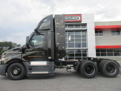 Semi truck cab and chassis in front of Freightliner dealership building. Door area shows text; may include branding and model details.