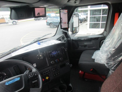 Truck cab interior with steering wheel, dashboard, and side mirror view; visible text on dashboard panels and controls.