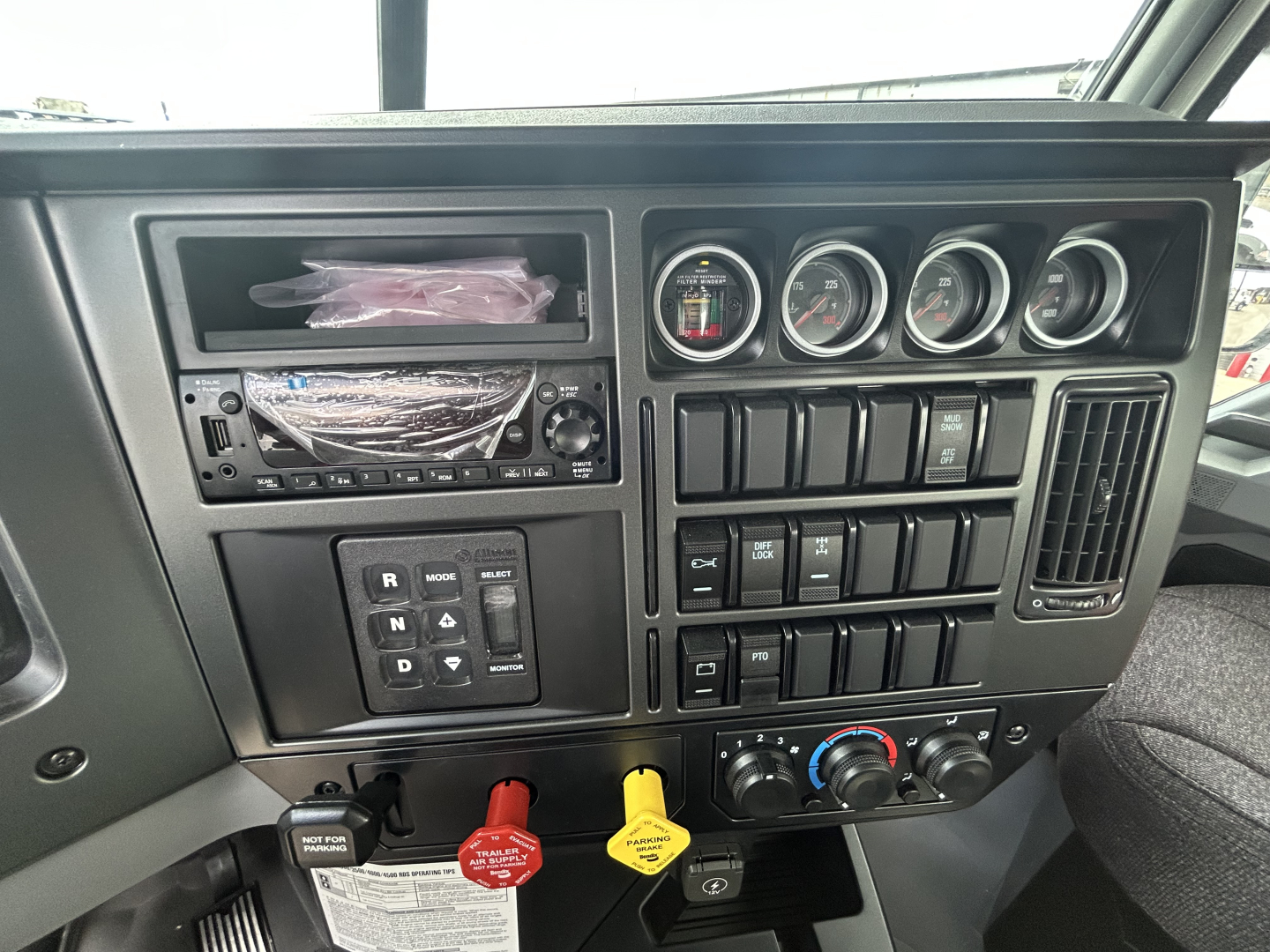 Dashboard view of a new Mack GR64B roll-off truck showing instrument gauges, control switches, and ignition area.