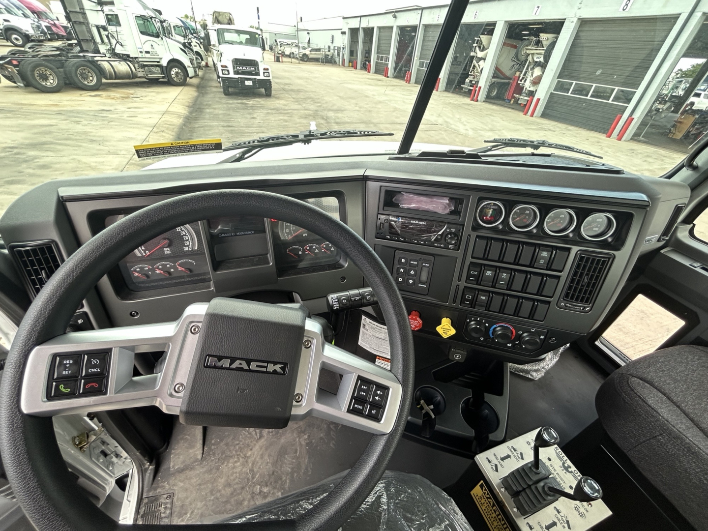 Dashboard and steering wheel of a Mack GR64B roll-off truck cab interior with gauges, switches, and control panels.