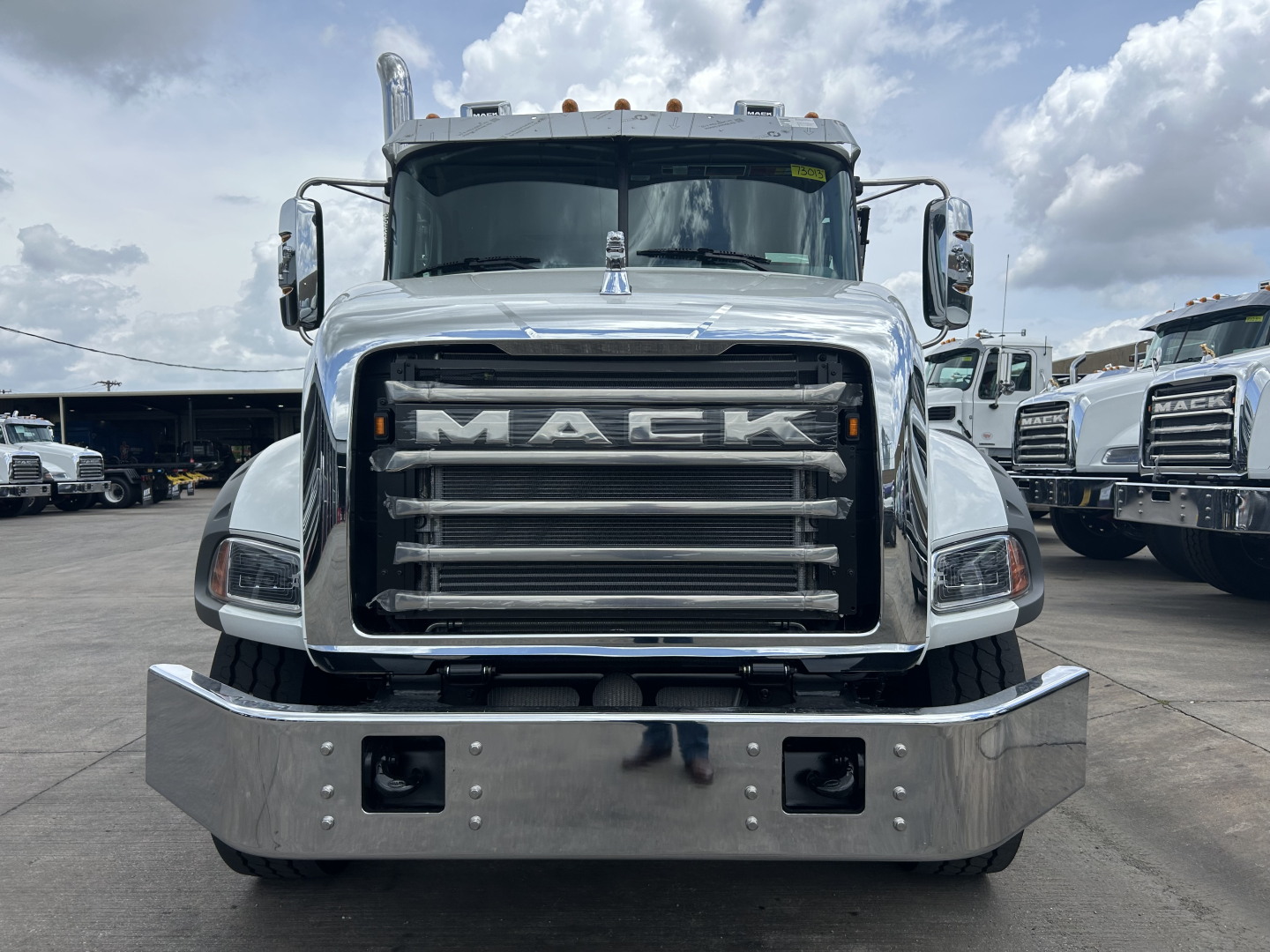 Front view of a new 2027 Mack GR64B roll-off truck showing large chrome grille with MACK lettering and chrome bumper.