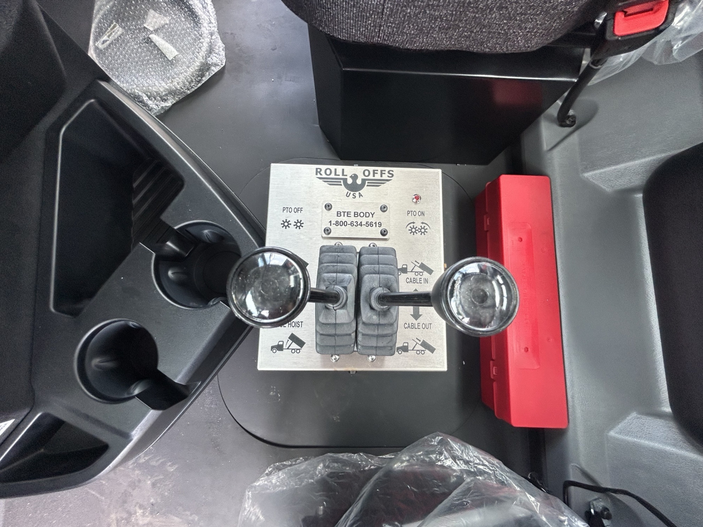 Label panel with Roll Offs controls and two round gauges in Mack GR64B cab area showing switches and warning icons.