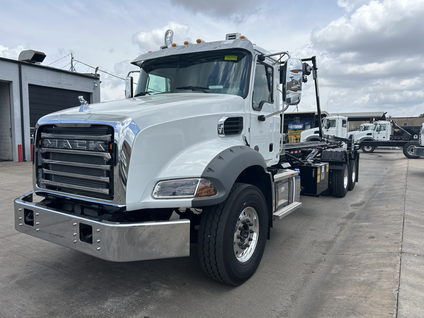 White Mack GR64B rolloff truck in side view showing front grille with 'MACK' badge and chrome bumper.