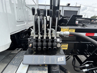 Truck control levers and hydraulic manifold on Mack GR64B rolof loader showing multiple levers and hydraulic hoses with caution labels.