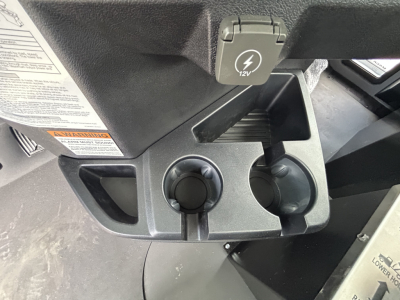 Dashboard area of a Mack GR64B showing two cup holders and a 12V power outlet cover with 12V icon.