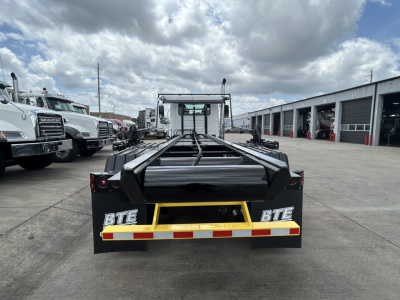 Rolloff truck bed of a 2027 Mack GR64B in a dealership lot, rear view showing BTE equipment on bumper and reflective safety stripe.