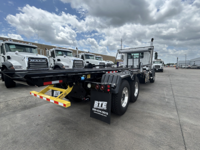 Truck chassis rear view showing dual rear axles and rear underride guard, with 'BTE' mudflaps and dealership contact info.