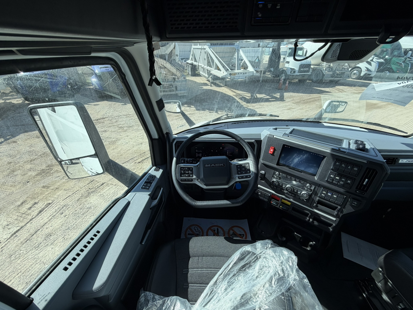 Interior of a Mack PR64T76H cab showing steering wheel, dashboard, and driver seat from a front-right viewpoint.