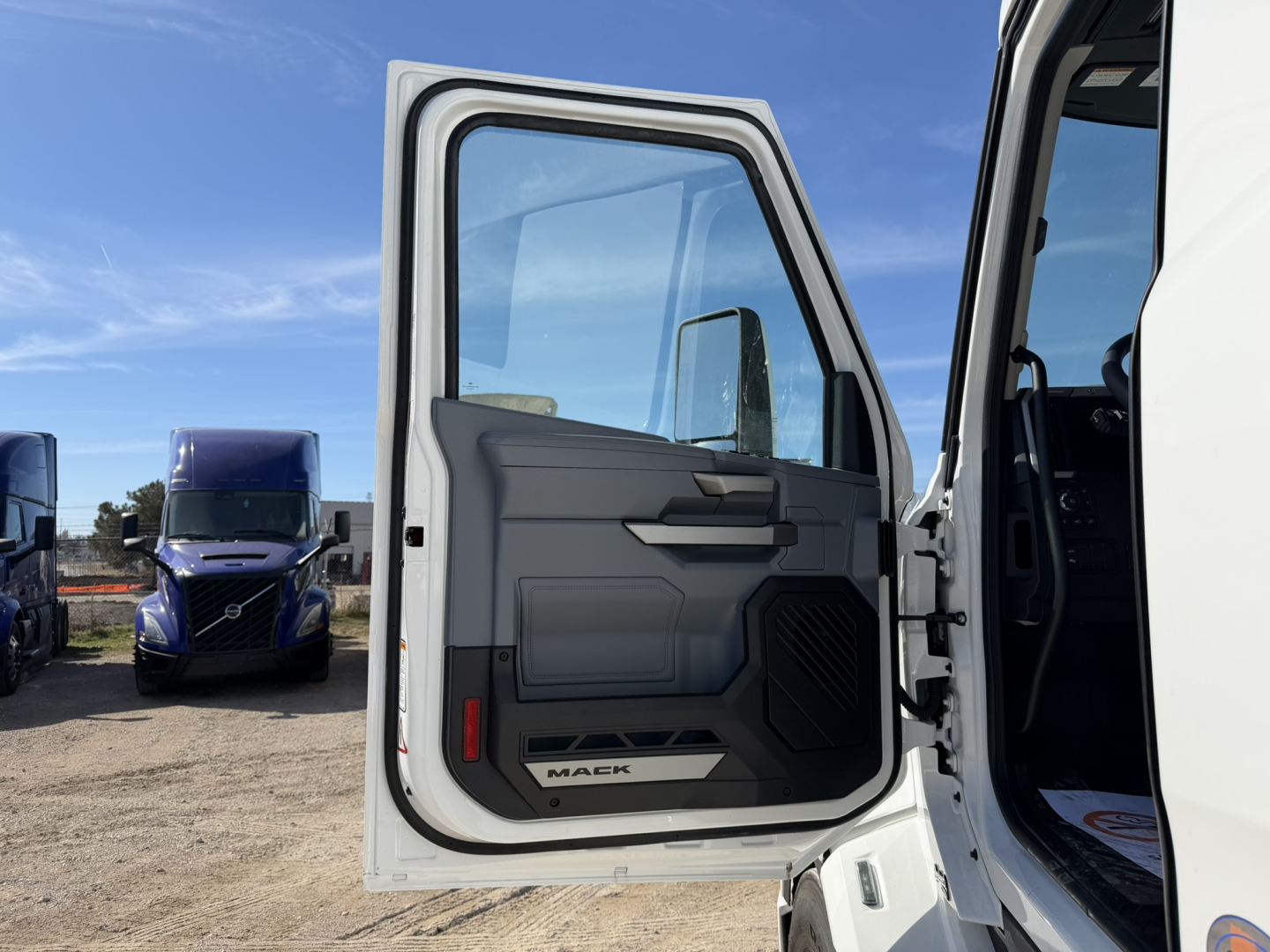 Truck cab door open showing interior panel and Mack badge on lower dash, exterior white cab in daylight.
