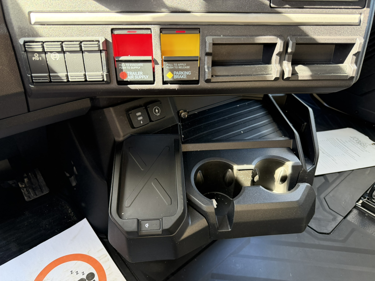 Cab interior of a new 2026 Mack PR64T76H showing cup holders and center console with storage tray and control panel.